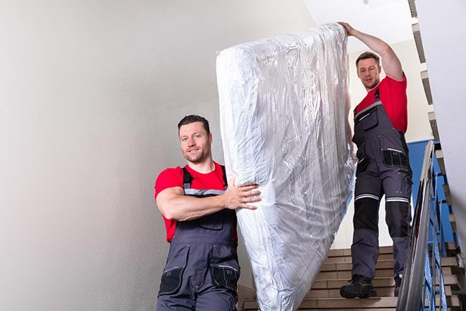 two people carrying a box spring out of a room in Greenville, SC